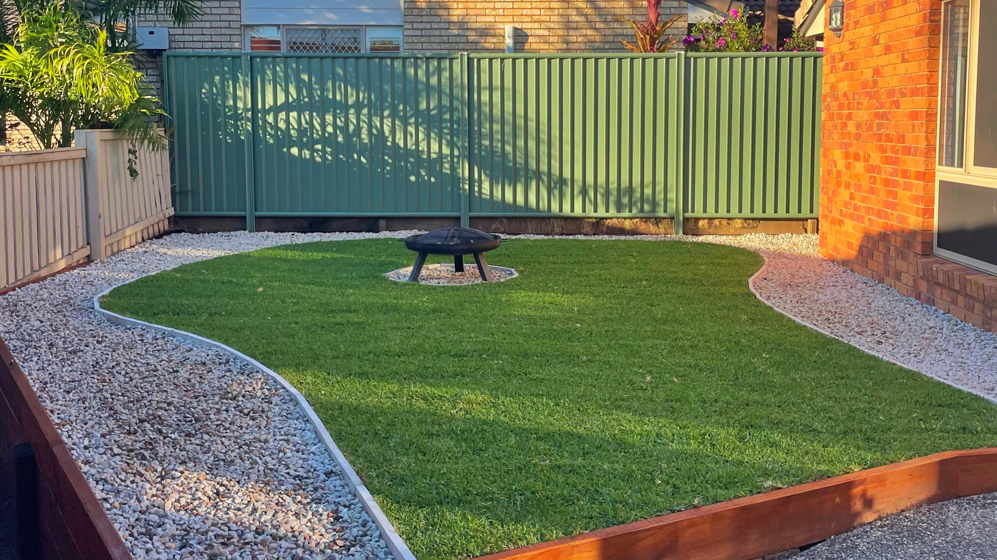 Level lawn with new sleeper retaining, pebble borders and a fire pit, finished at golden hour on the Sunshine Coast