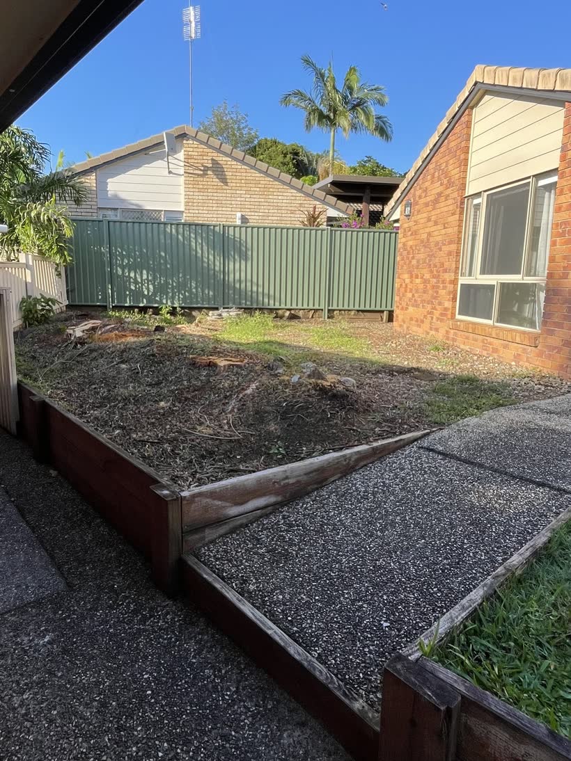 Bare sloping dirt and old timber sleepers before the yard was levelled